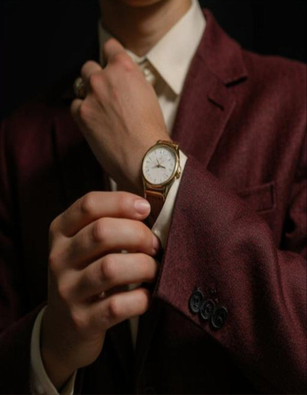 Person wearing a burgundy suit with a watch on their wrist.